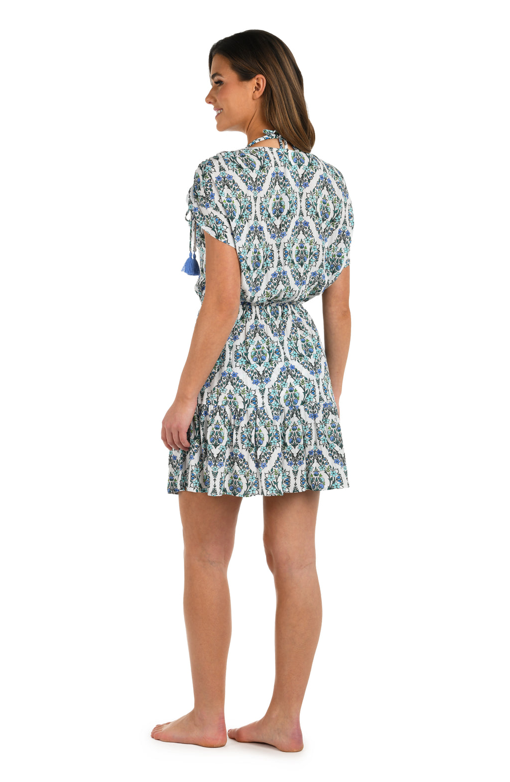 Full body side image of model wearing a blue and white geometric patterned V-neck short cover up dress. 