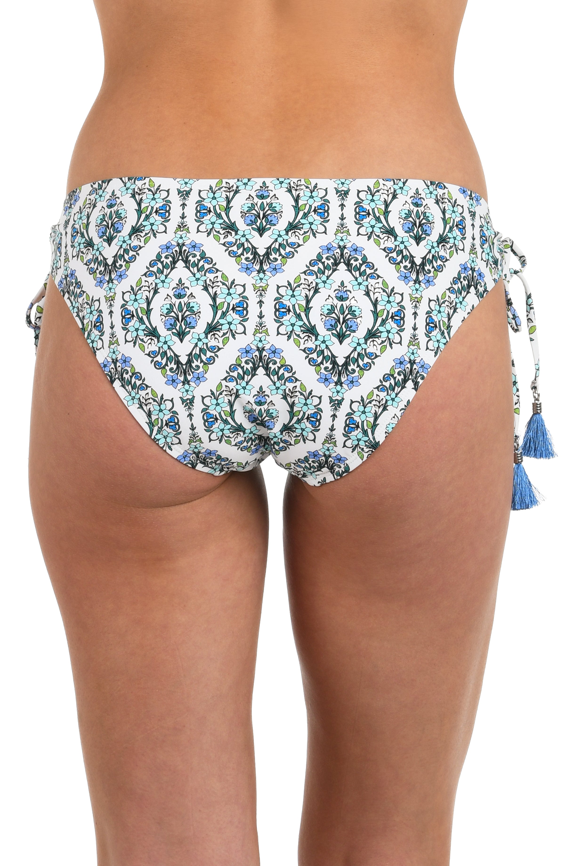 Back image of model wearing hipster bikini bottoms with a blue and green tile-inspired print, featuring side ties, tassels, and moderate rear coverage.