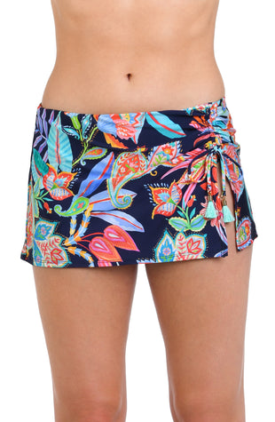 Model is wearing a pink, orange, yellow, and green multicolored tropical patterned skirted bottom against an indigo blue background.
