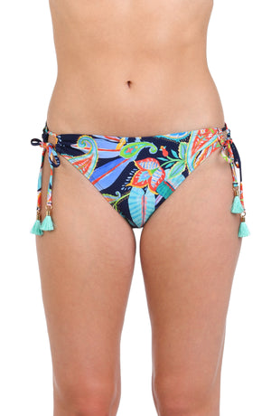 Model is wearing a pink, orange, yellow, and green multicolored tropical patterned side tie hipster bottom against an indigo blue background.
