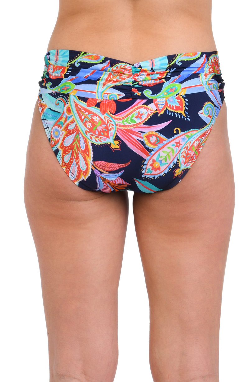 Model is wearing a pink, orange, yellow, and green multicolored tropical patterned hipster bottom against an indigo blue background.