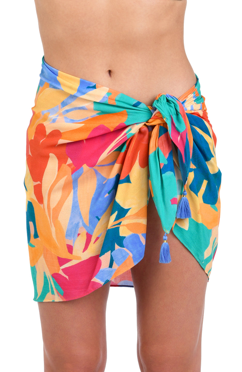 Model is wearing an orange, pink, blue, and aqua multicolored tropical patterned short pareo wrap cover up.