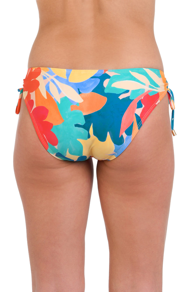 Model is wearing an orange, pink, blue, and aqua multicolored tropical patterned side tie hipster bikini bottom.