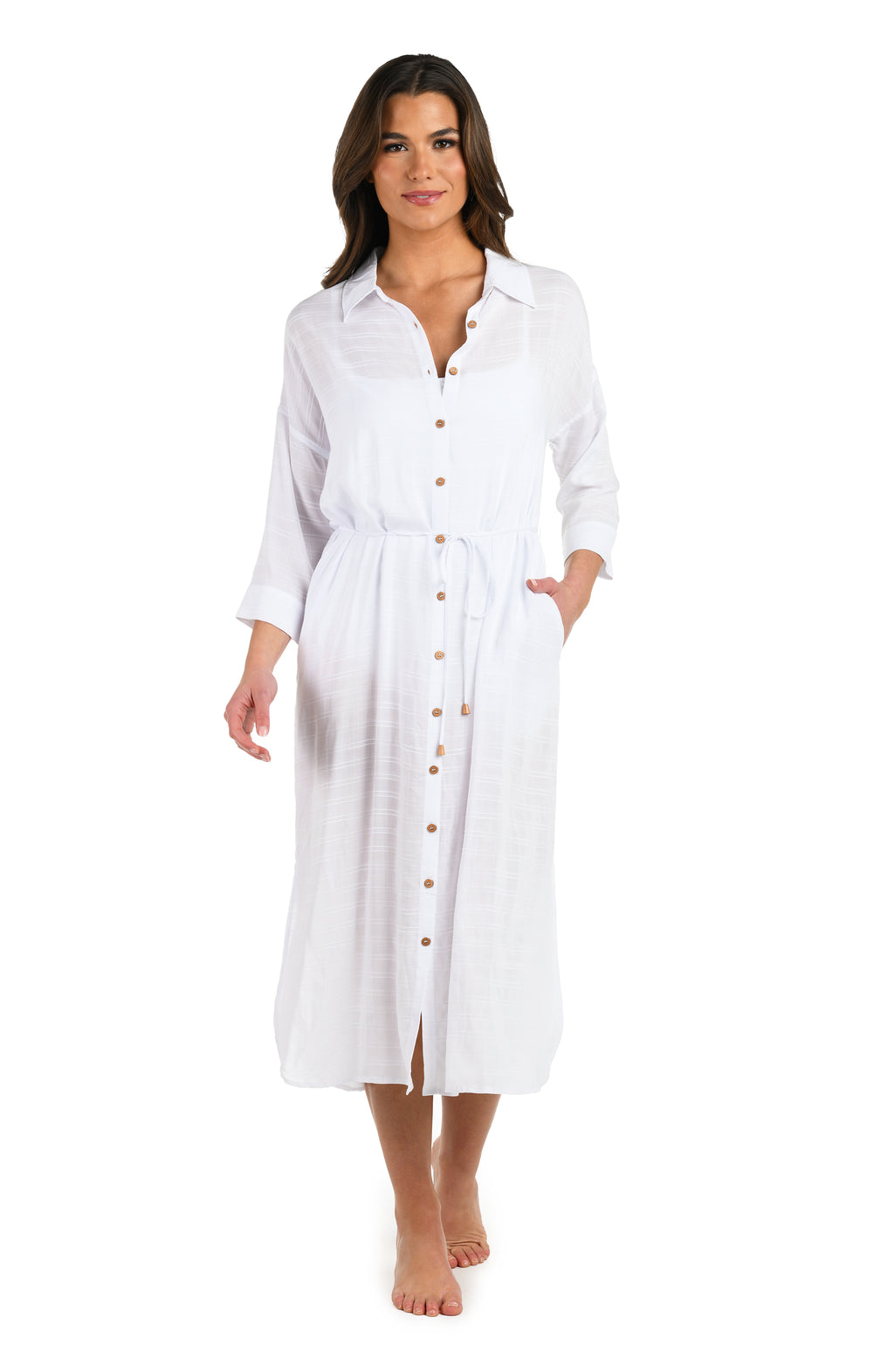 Full body front image of model wearing a white, long-sleeve, button-down midi beach cover-up dress with a drawstring waist and side slits.