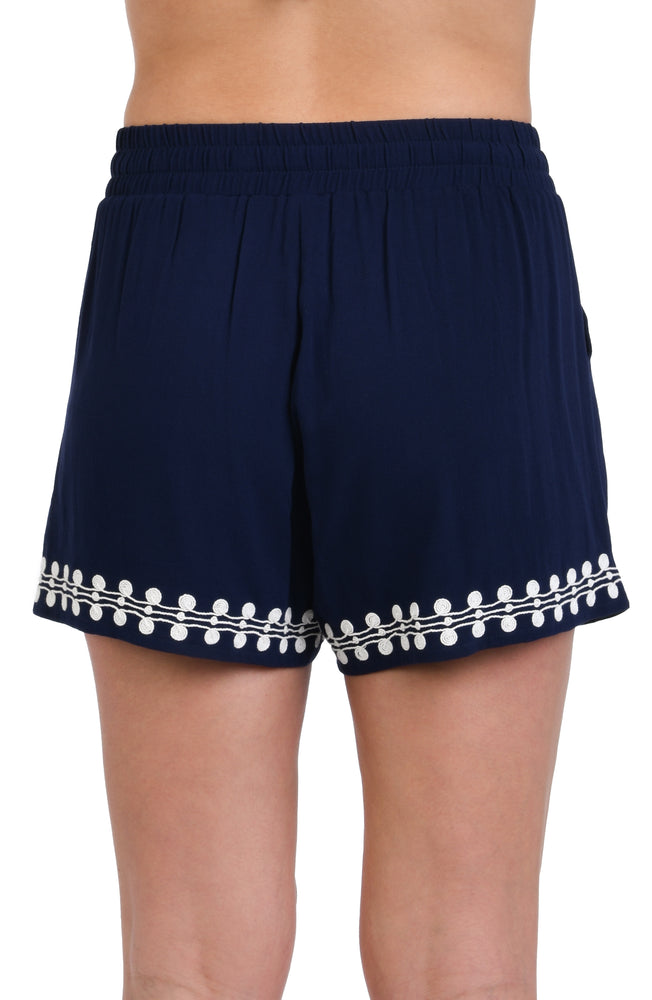 Model is wearing an indigo and white patterned beach shorts that resembles a string of white sea scallop shells.