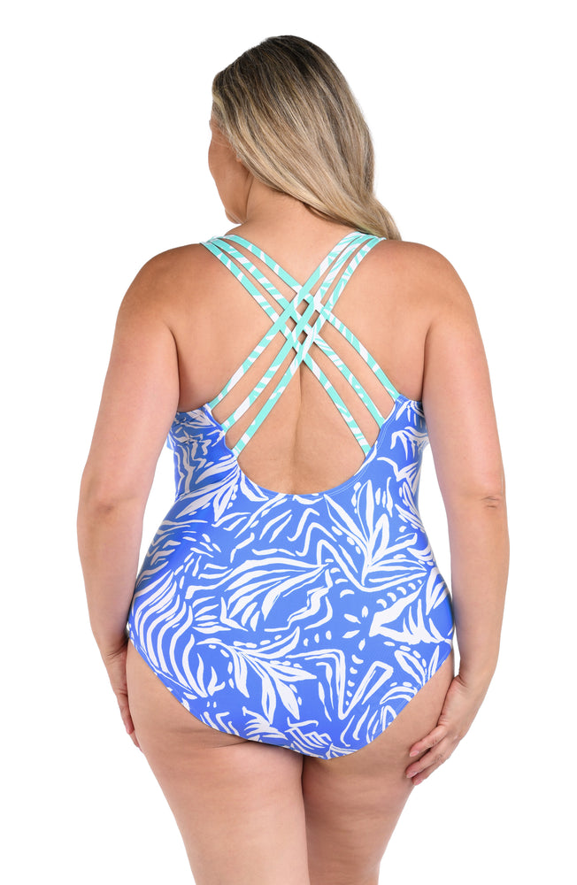 Model is wearing a two-toned one piece swimsuit with bold white botanical motifs on a background of contrasting shades of blue.