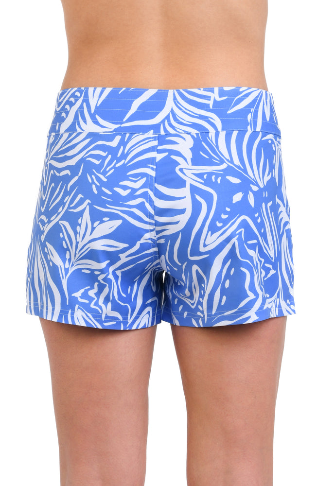 Model is wearing a two-toned board short bottom with bold white botanical motifs on a background of contrasting shades of blue.