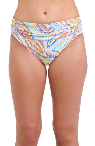 Model is wearing a geometric patterned hipster bikini bottom in pastel shades of pink, blue, and yellow, accented with sporadic glimmers of gold sequin-like details on a white background.