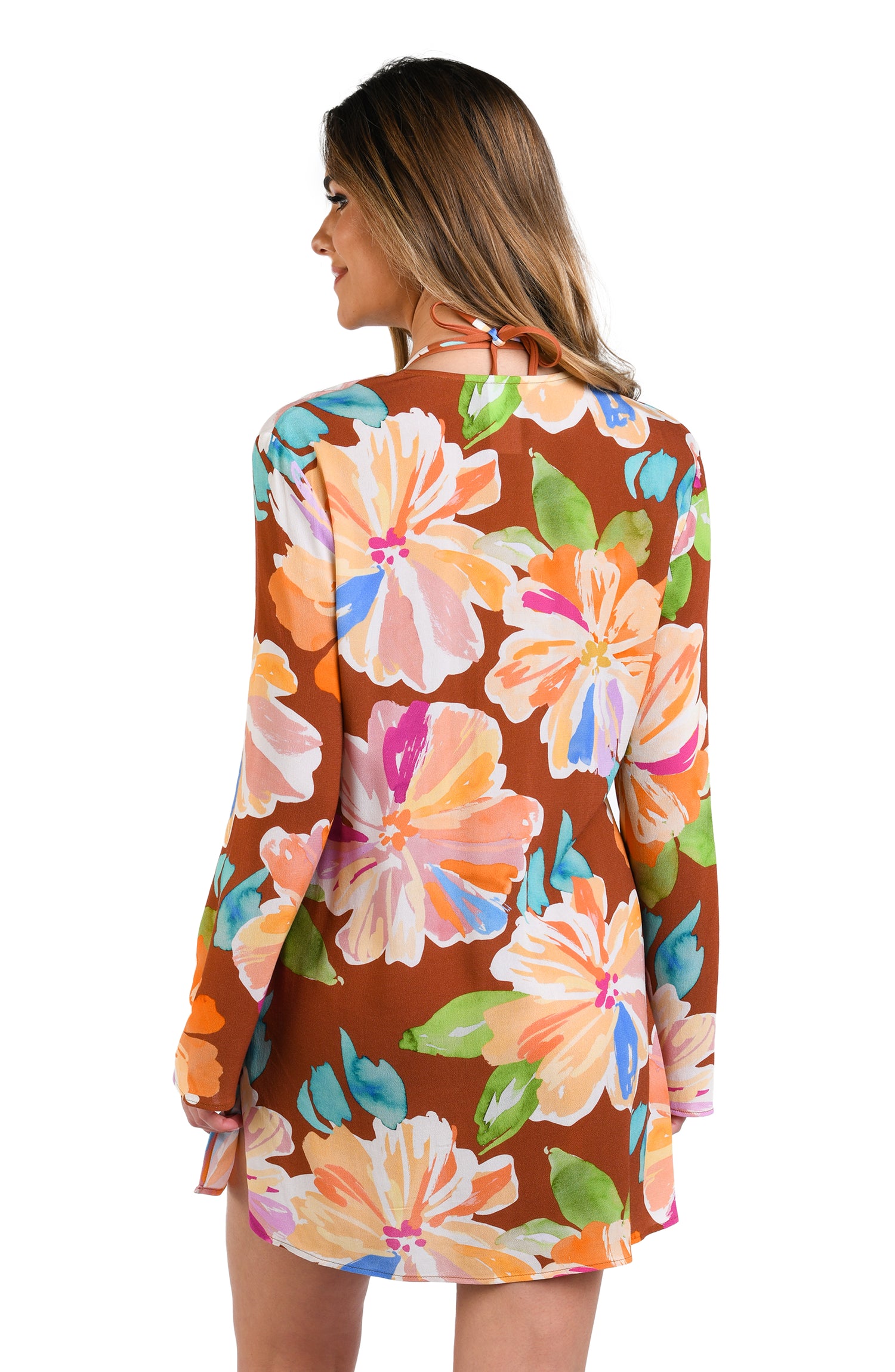 Model is wearing floral patterned tunic cover up with bold strokes of peach, pink, orange, and blue hues on a rich brown background.