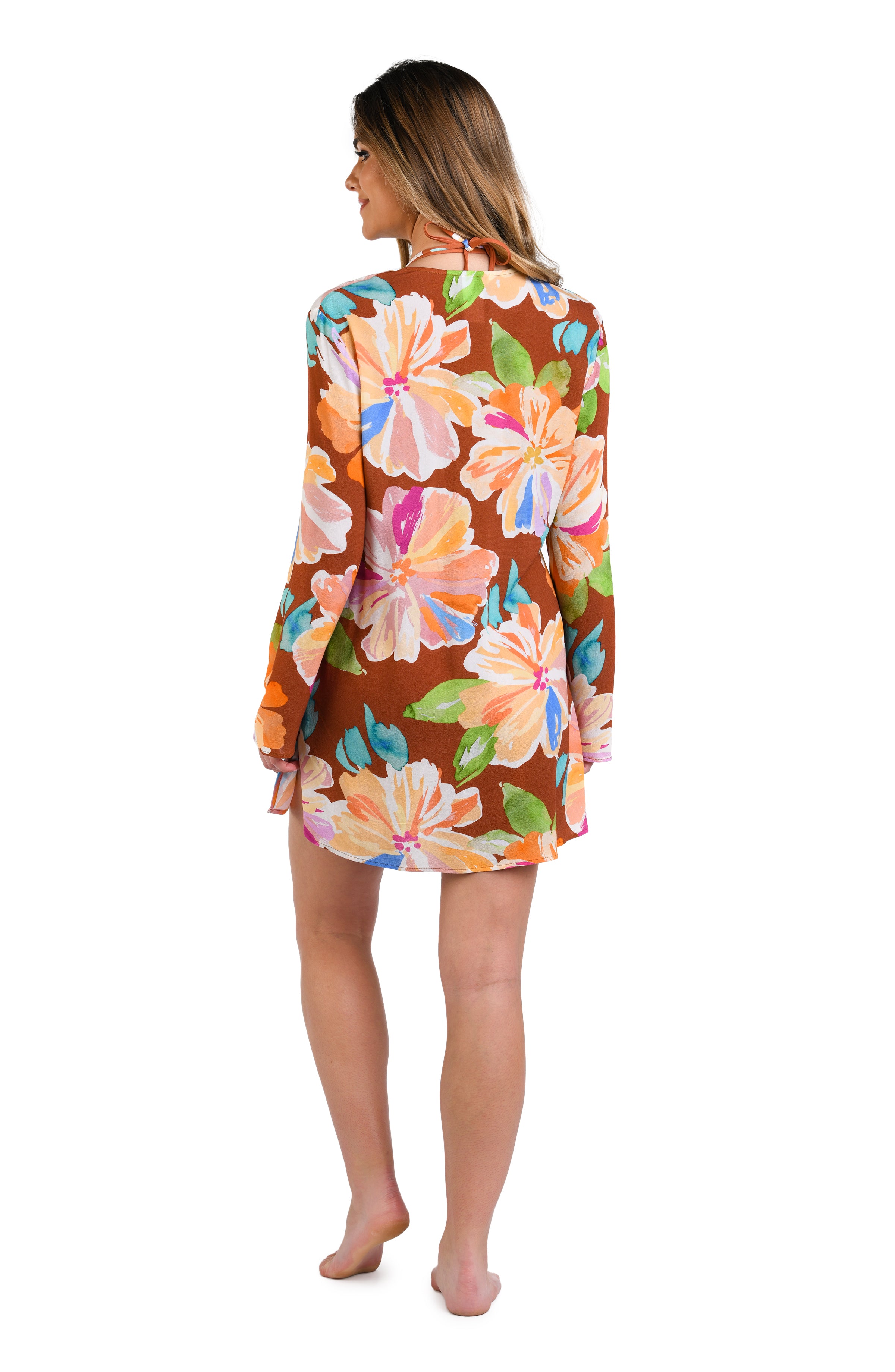 Model is wearing floral patterned tunic cover up with bold strokes of peach, pink, orange, and blue hues on a rich brown background.