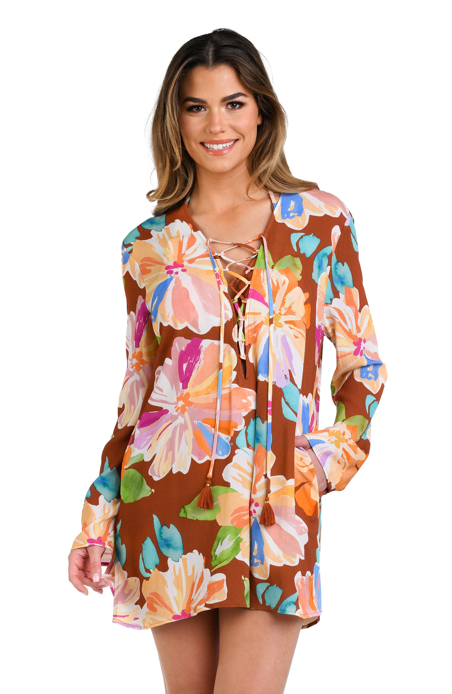 Model is wearing floral patterned tunic cover up with bold strokes of peach, pink, orange, and blue hues on a rich brown background.