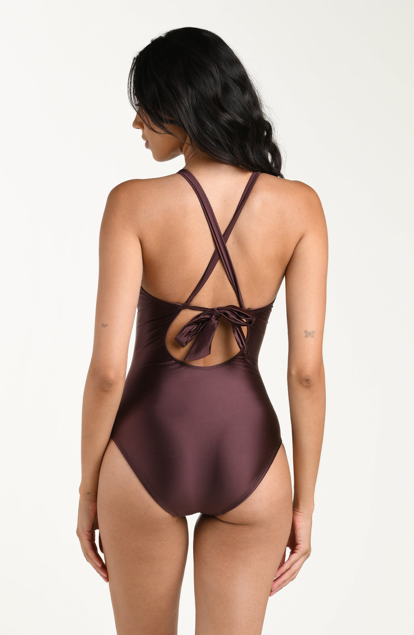 
                  
                    Back image of model wearing a truffle (brown) colored one-piece swimsuit with crisscross straps and a tie-back detail above a small cutout, and moderate rear coverage.
                  
                