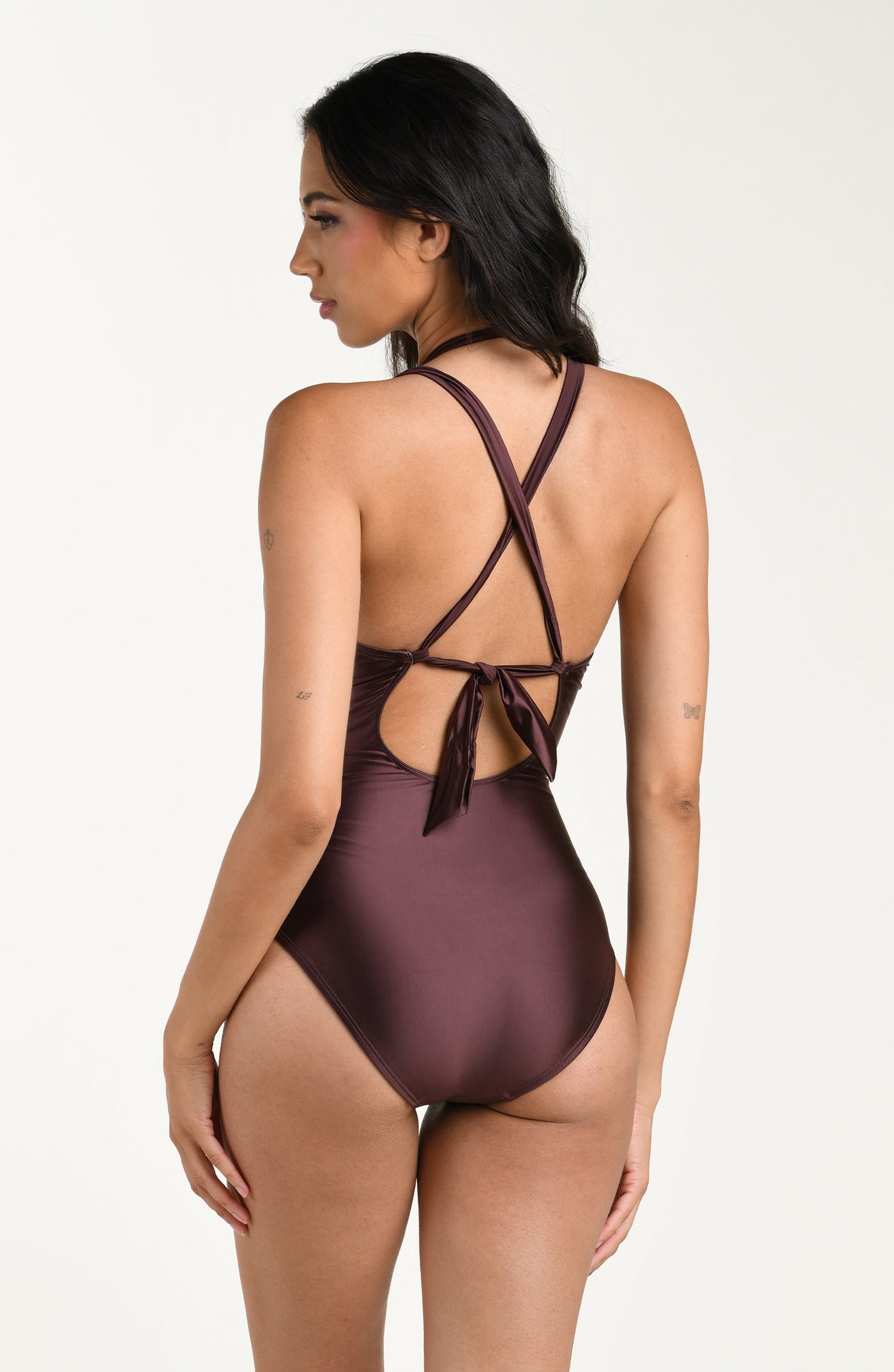 
                  
                    Back image of model wearing a truffle (brown) colored one-piece swimsuit with crisscross straps, a tie-back detail above a small cutout, and moderate rear coverage.
                  
                