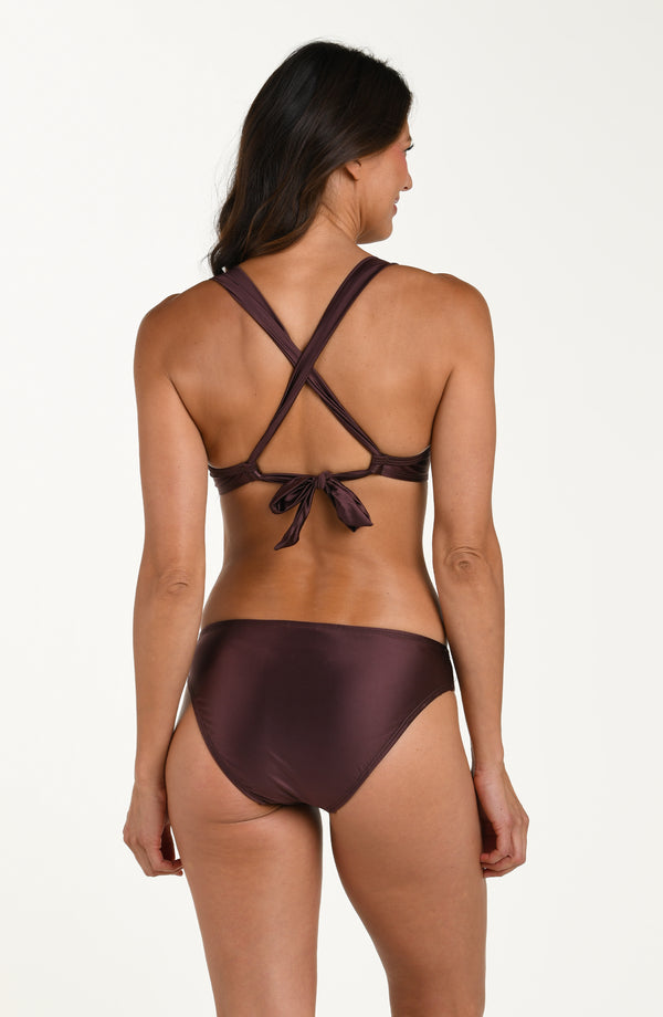 Full body back image of model wearing a halter bikini top in a truffle (brown) color with ruched triangle featuring wide straps that crisscross and tie at the lower back. This is paired with matching bikini bottoms. 