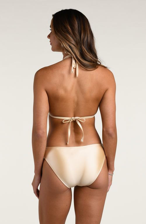 Woman wearing a champagne colored bikini top and matching bottom against a white background. 