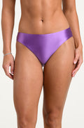 Woman wearing a lavender colored bikini bottoms against a white background. 