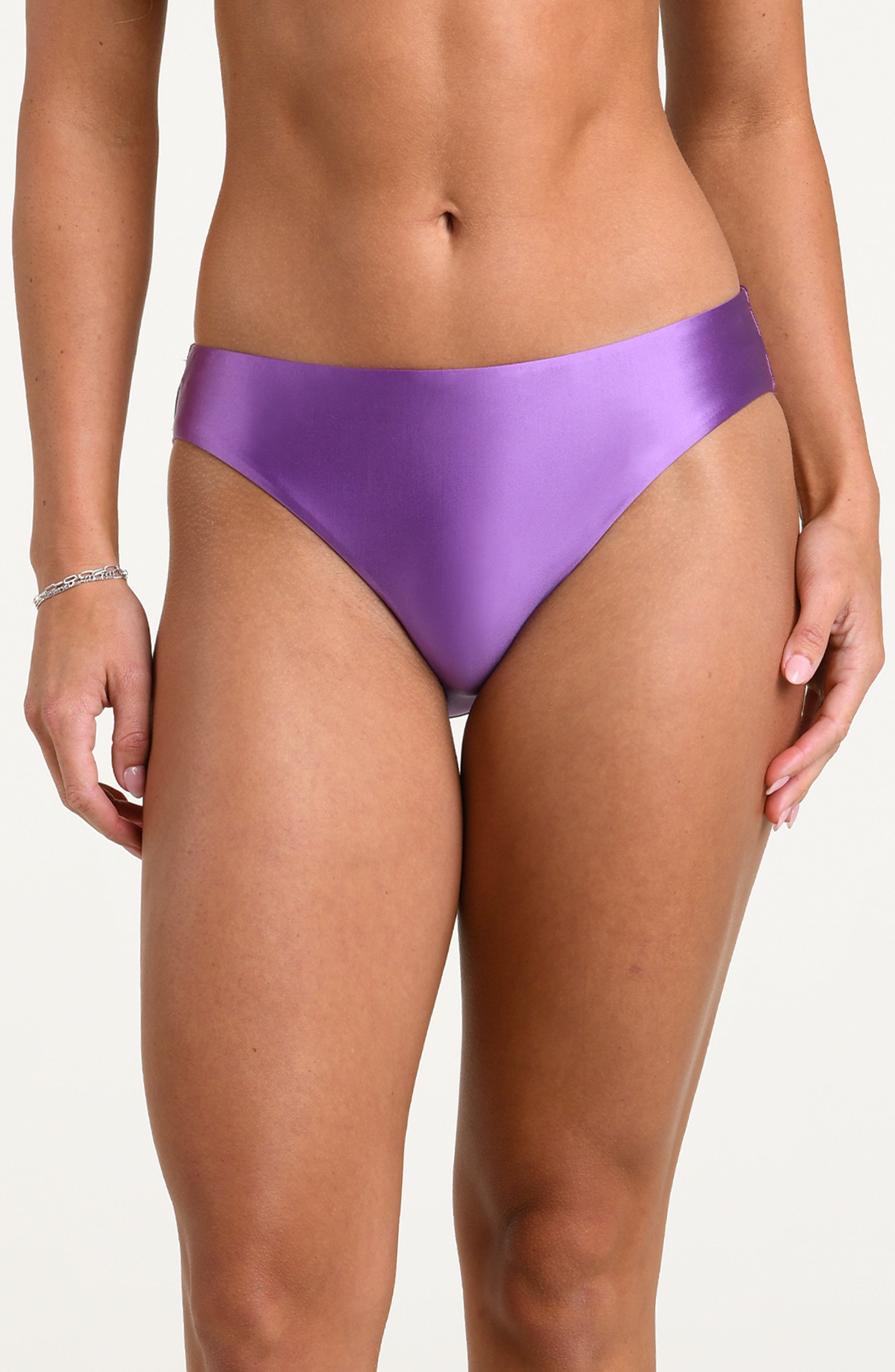 Woman wearing a lavender colored bikini bottoms against a white background. 