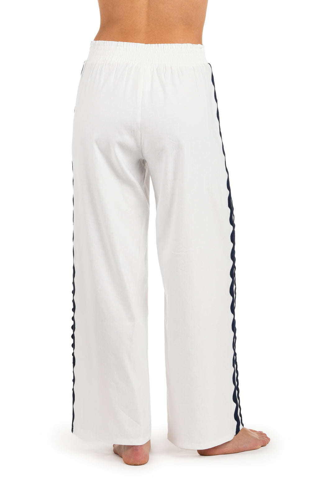 Close-up back image of model wearing a white wide-leg cover-up pants with an elastic waistband and navy blue wavy trim along the side seams.