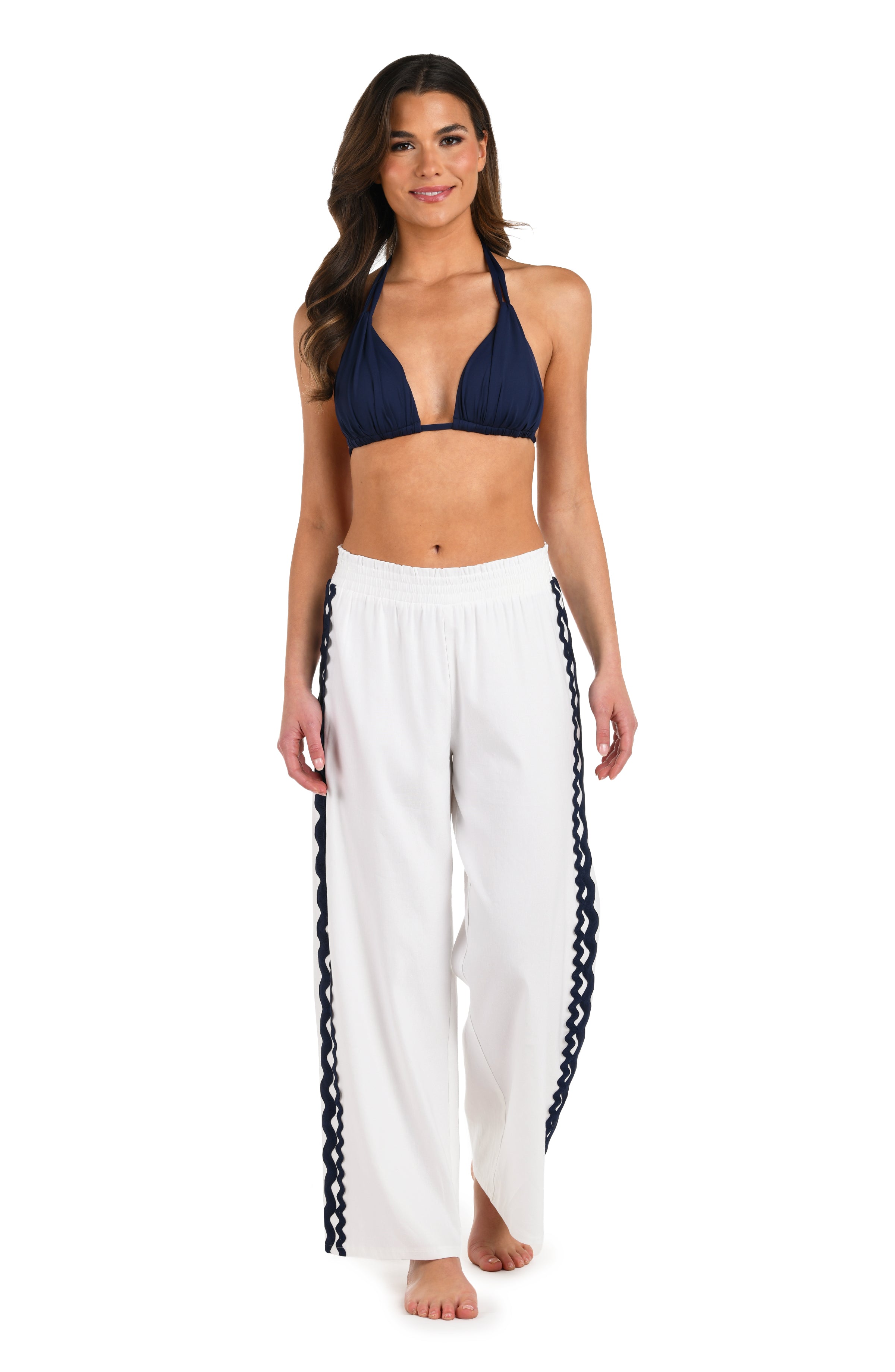 Full body front image of model wearing a white wide-leg cover-up pants with an elastic waistband and navy blue wavy trim along the side seams.