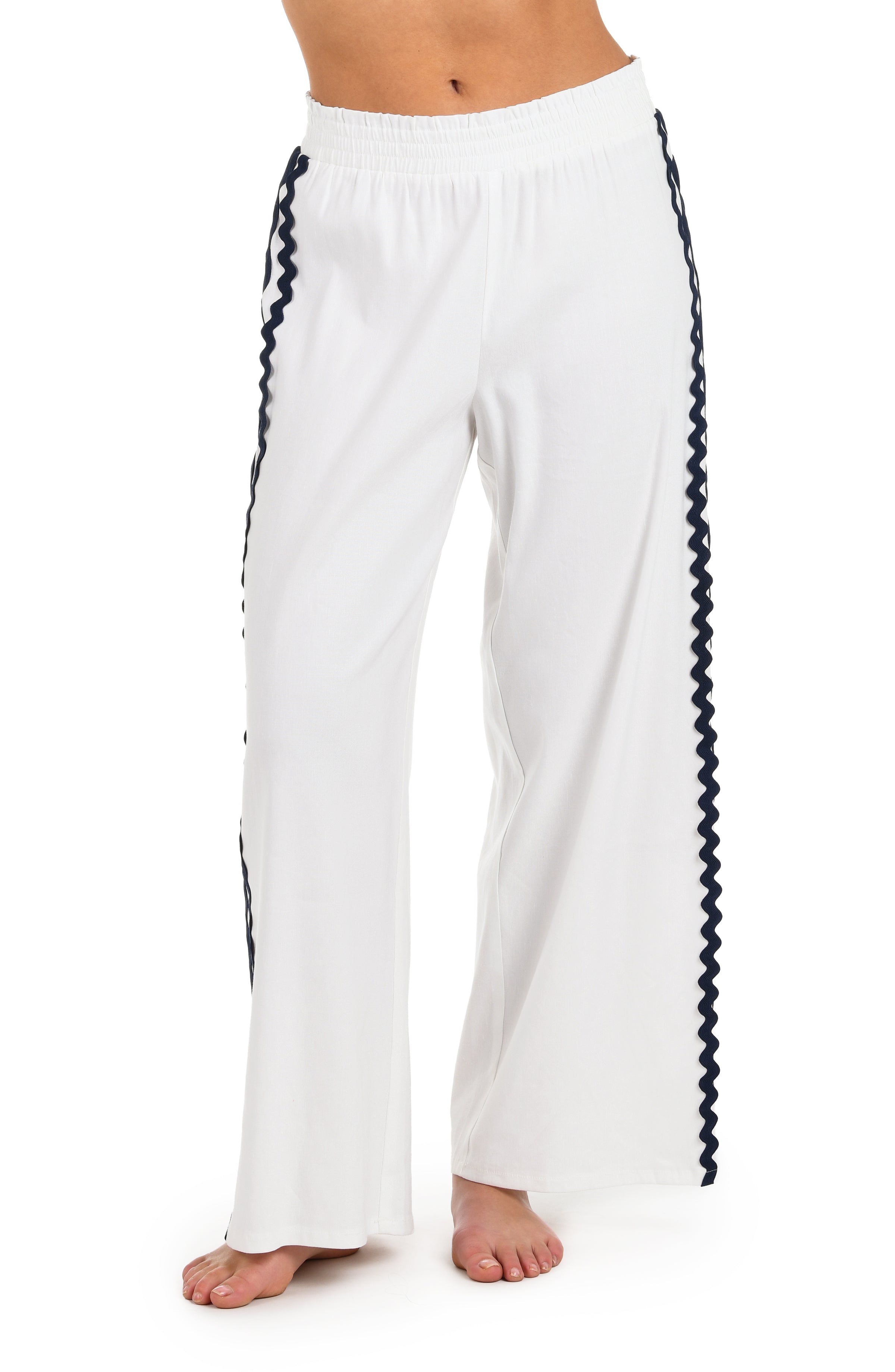 Close-up front image of model wearing a white wide-leg cover-up pants with an elastic waistband and navy blue wavy trim along the side seams.