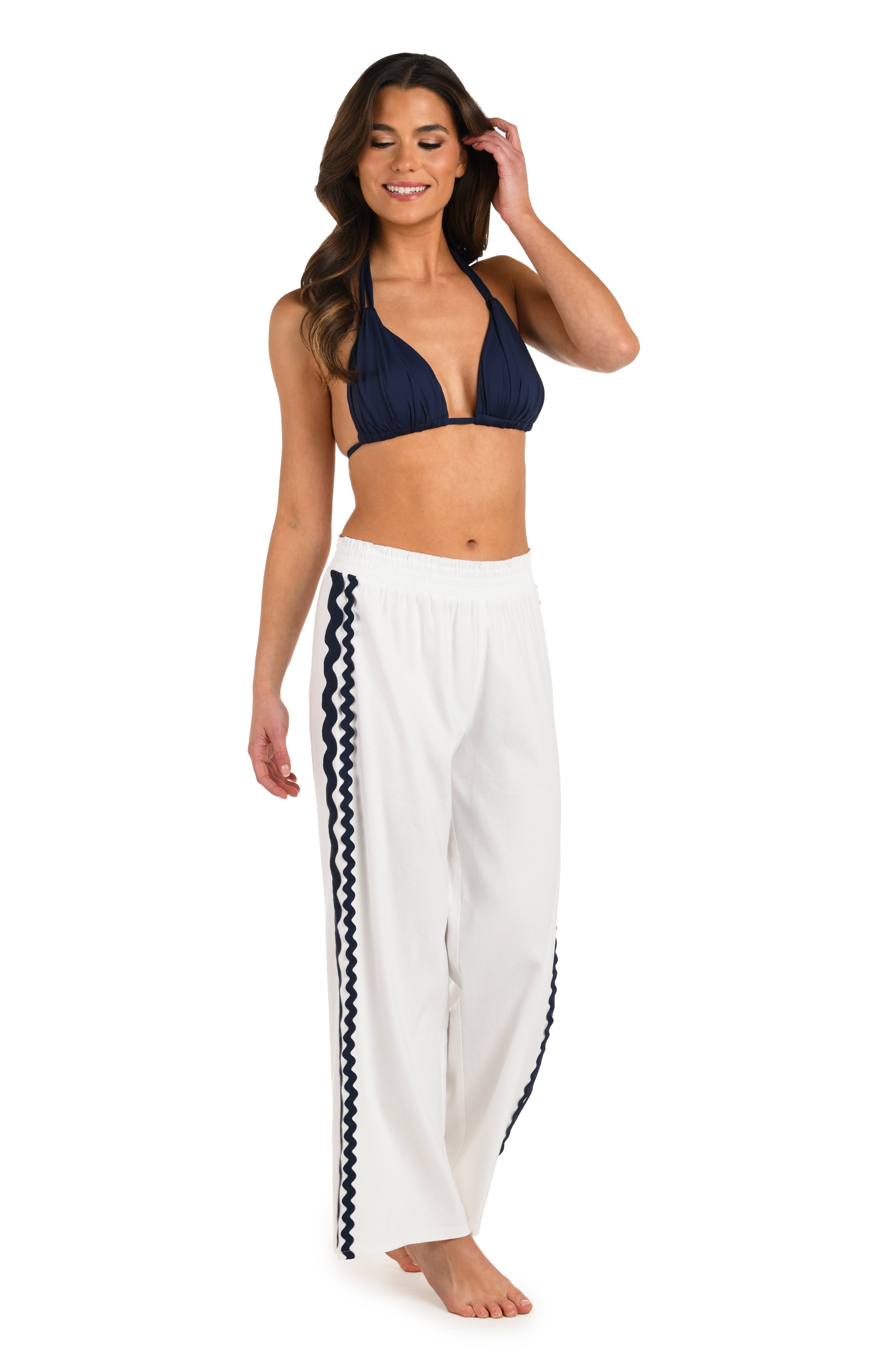 Full body front image of model wearing a white wide-leg cover-up pants with an elastic waistband and navy blue wavy trim along the side seams.