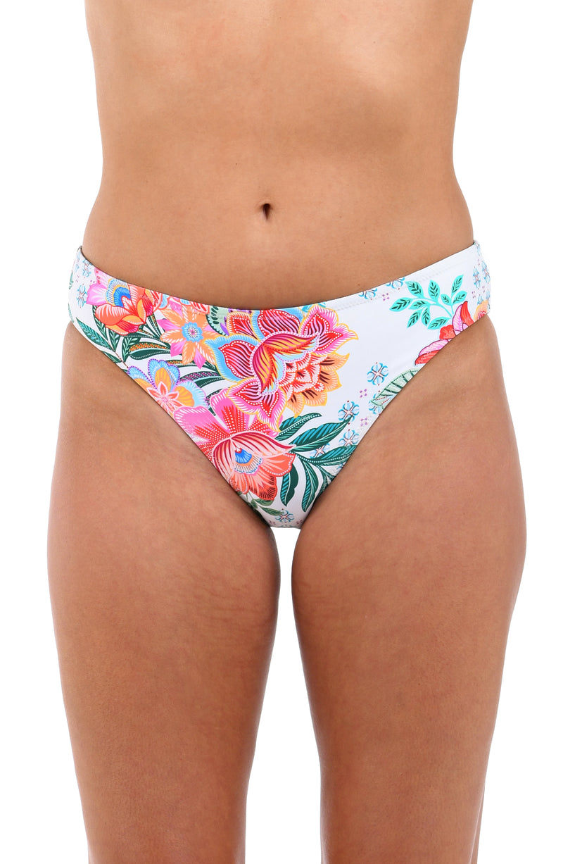 Front image of model wearing the Riviera Resort Reversible Hipster Bottom in a white multi colored tropical print.