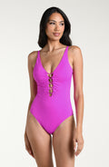 Woman wearing a violet colored one piece swimsuit with a plunging neckline against a white background