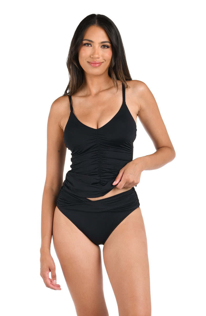 Model is wearing a solid black over-the-shoulder tankini swimsuit top.