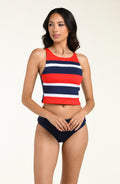 Woman wearing a red, white, and blue striped bikini top and navy blue bottom against a beige background