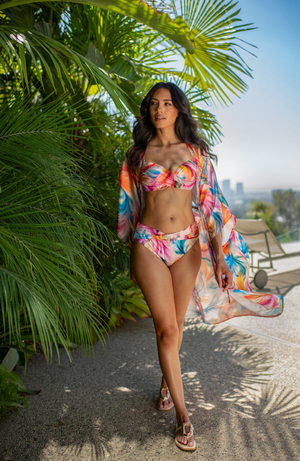 Lifestyle image of model wearing a multicolored feather printed long kimono-style cover-up featuring wide sleeves and a drawstring waist.