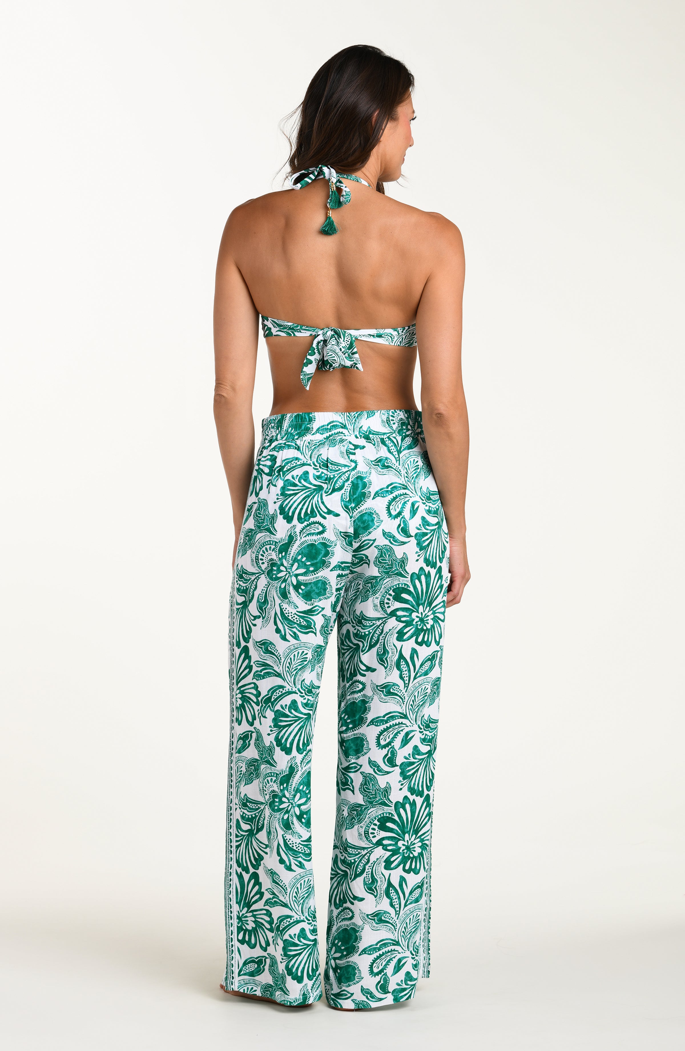 Woman wearing a green bikini top and leaf-patterned pants on a white background