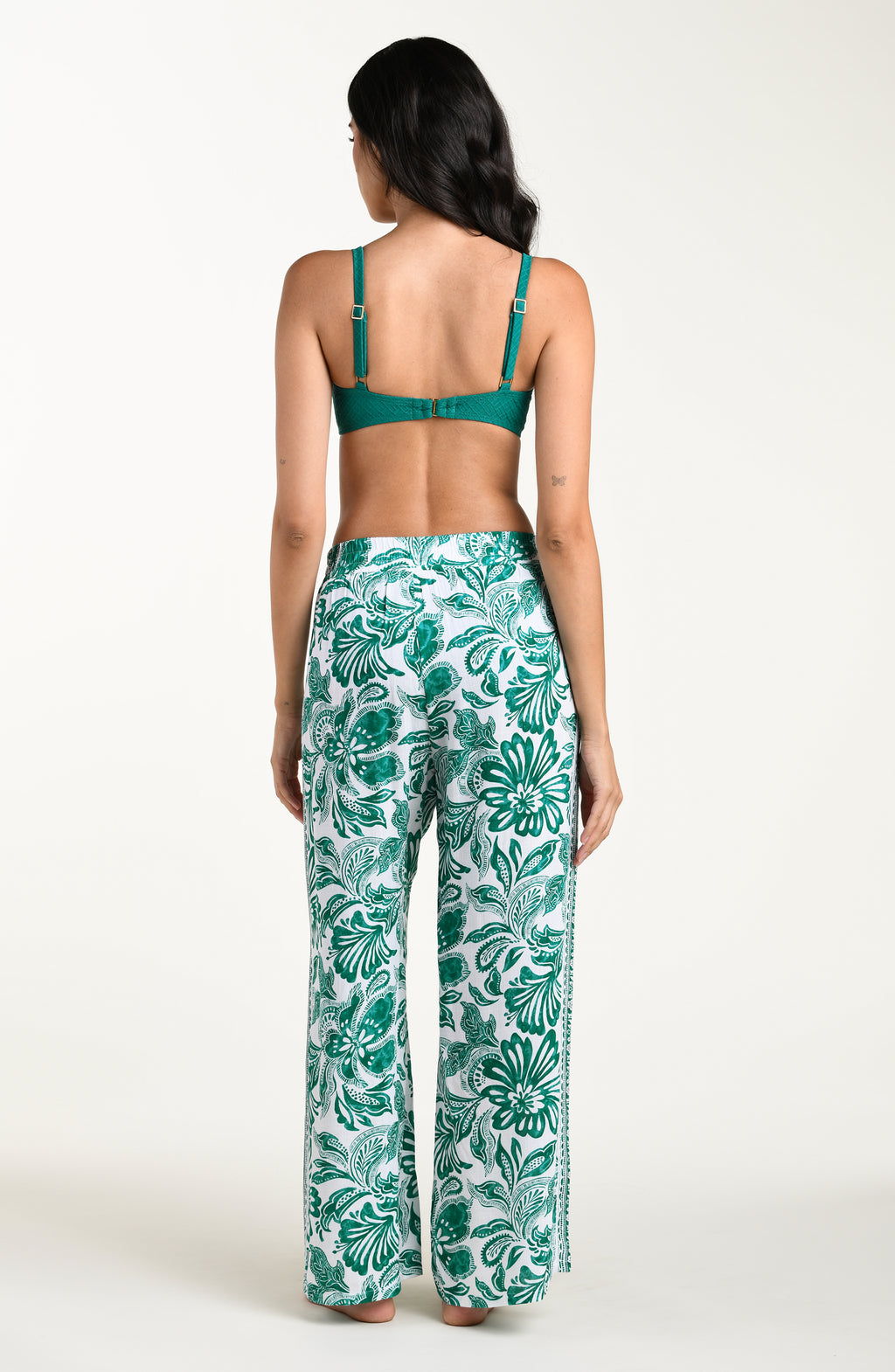 Woman wearing a green bikini top and leaf-patterned pants on a white background