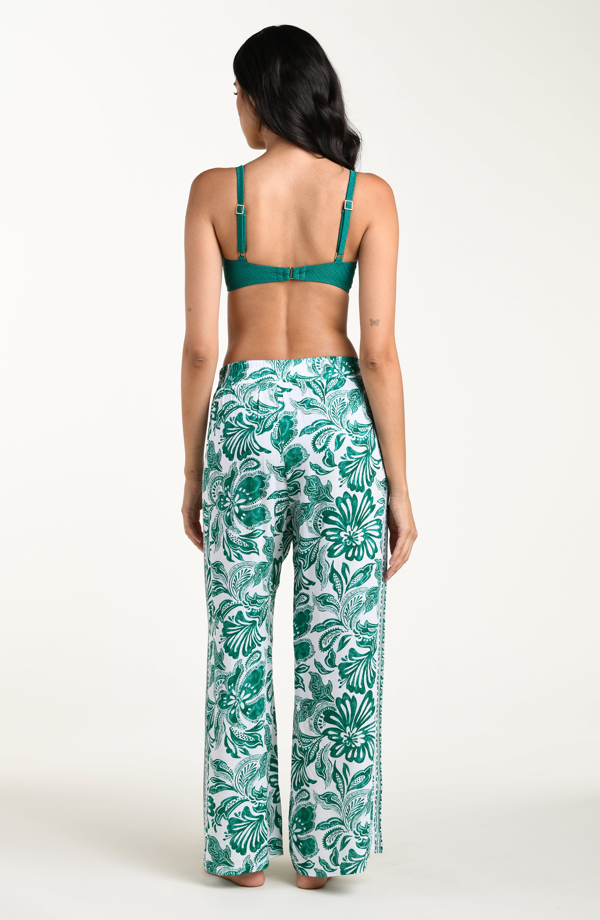 Woman wearing a green bikini top and leaf-patterned pants on a white background