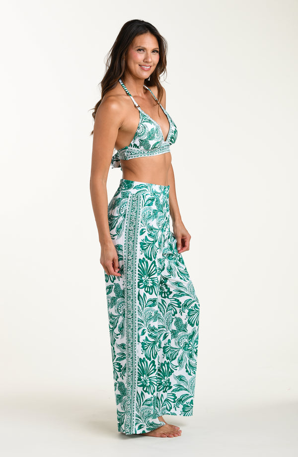 Woman wearing a green bikini top and leaf-patterned pants on a white background