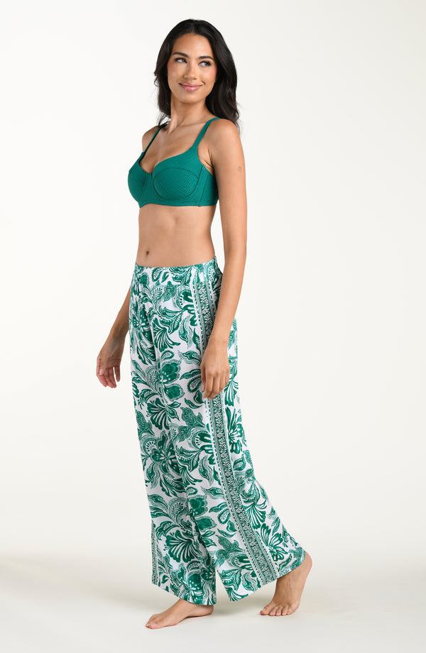 Woman wearing a green bikini top and leaf-patterned pants on a white background