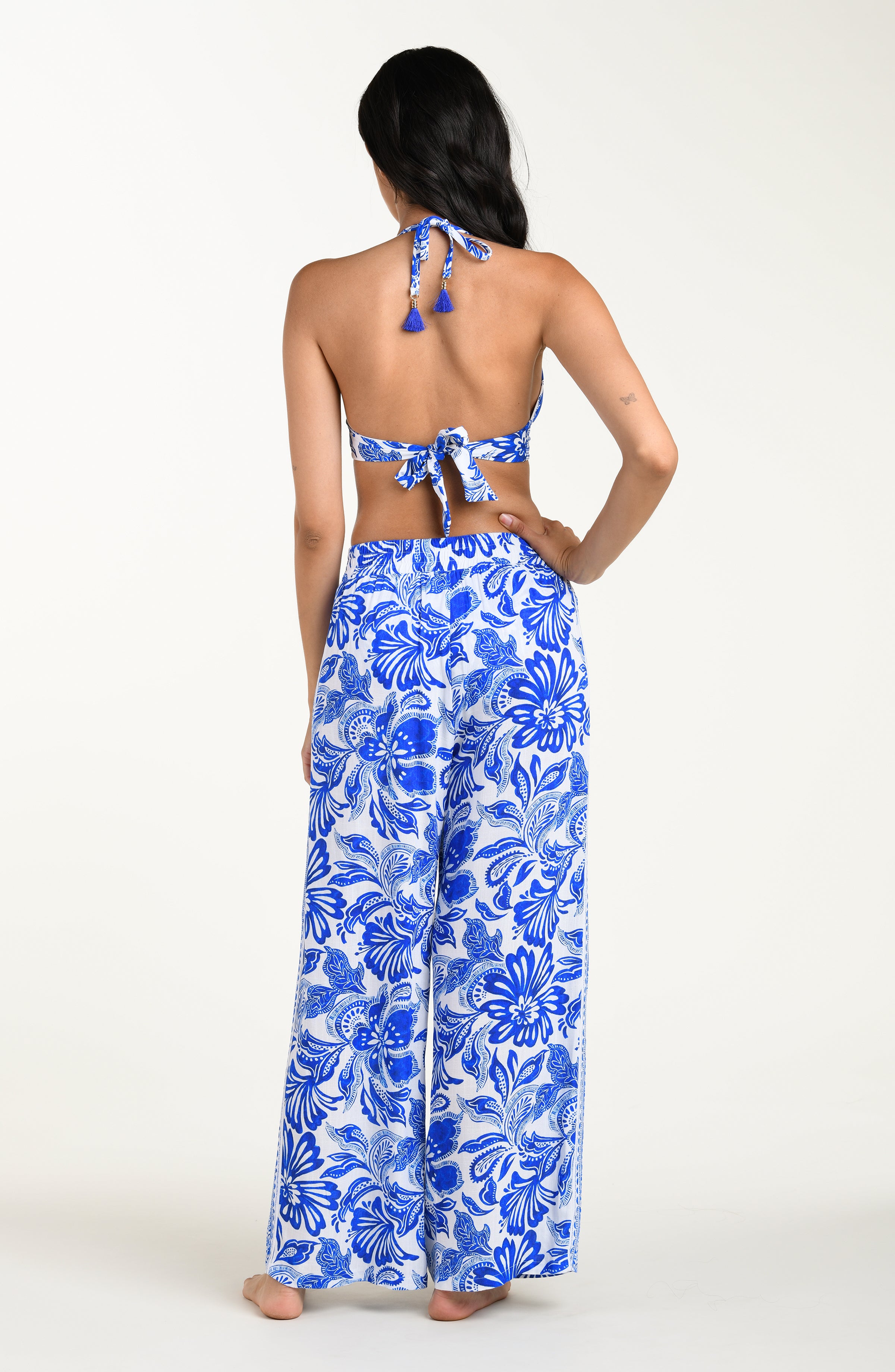 Woman wearing a blue floral bikini top and wide-leg pants on a white background