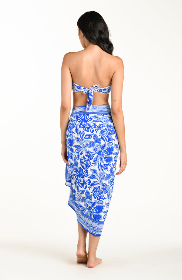 Woman wearing a blue floral patterned bikini top and matching sarong on a white background