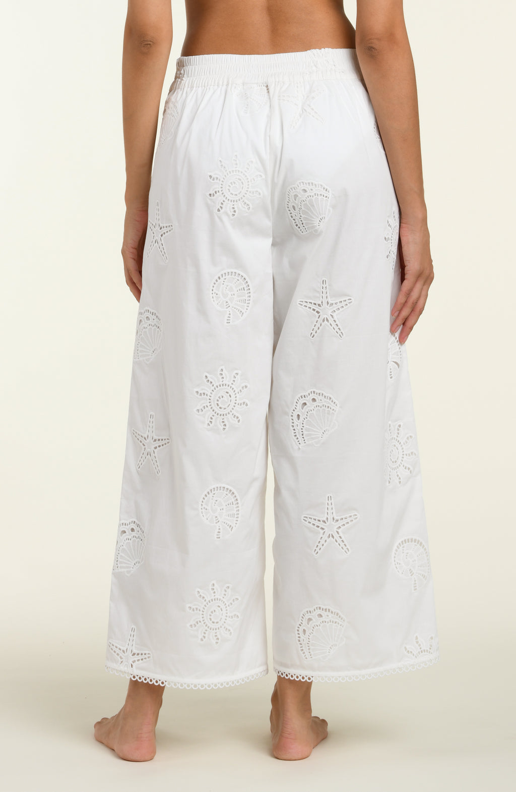 Woman wearing white cover up pants against a white background. 