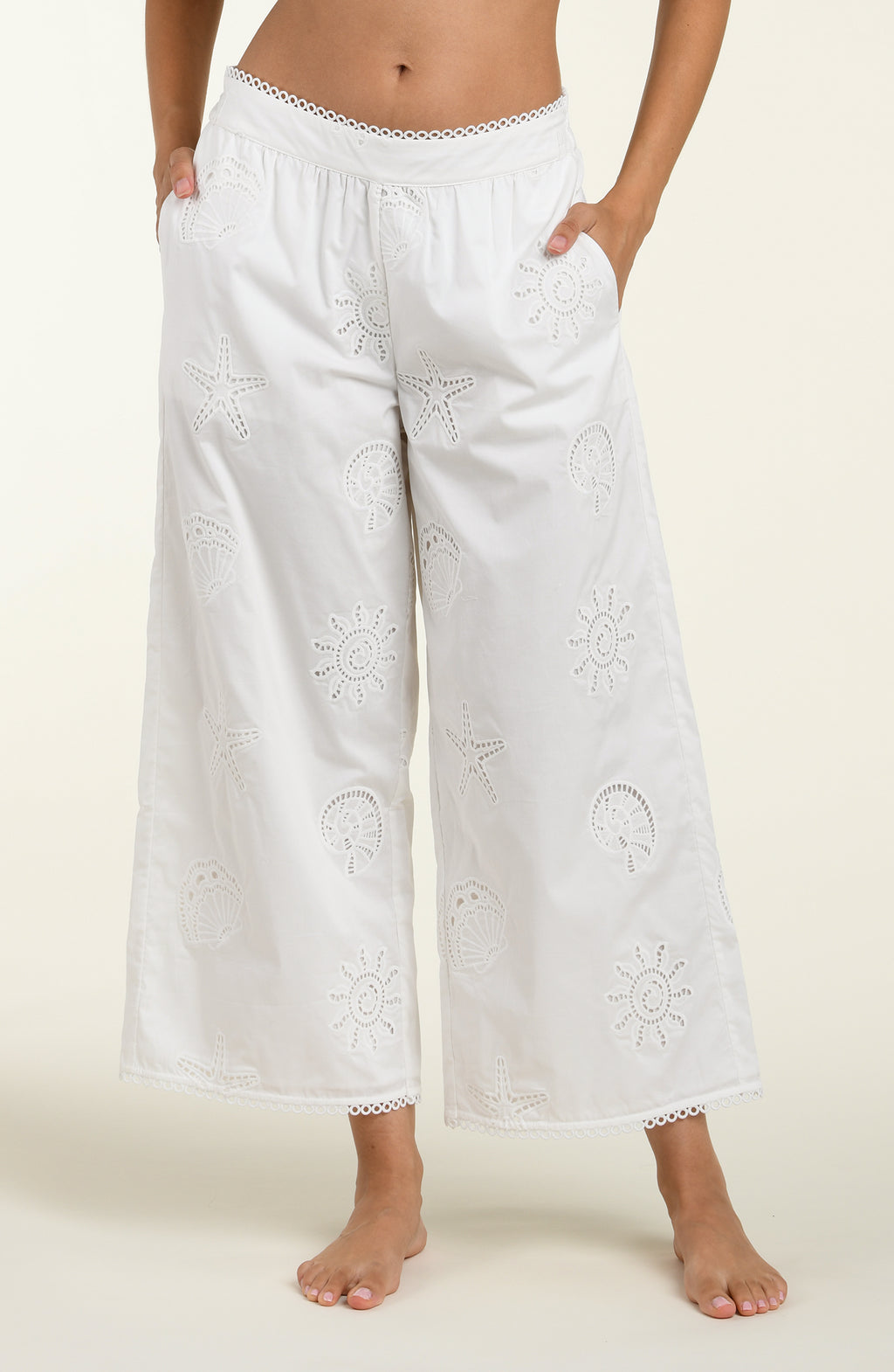 Woman wearing white cover up pants against a white background. 