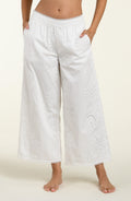 Woman wearing white cover up pants against a white background. 