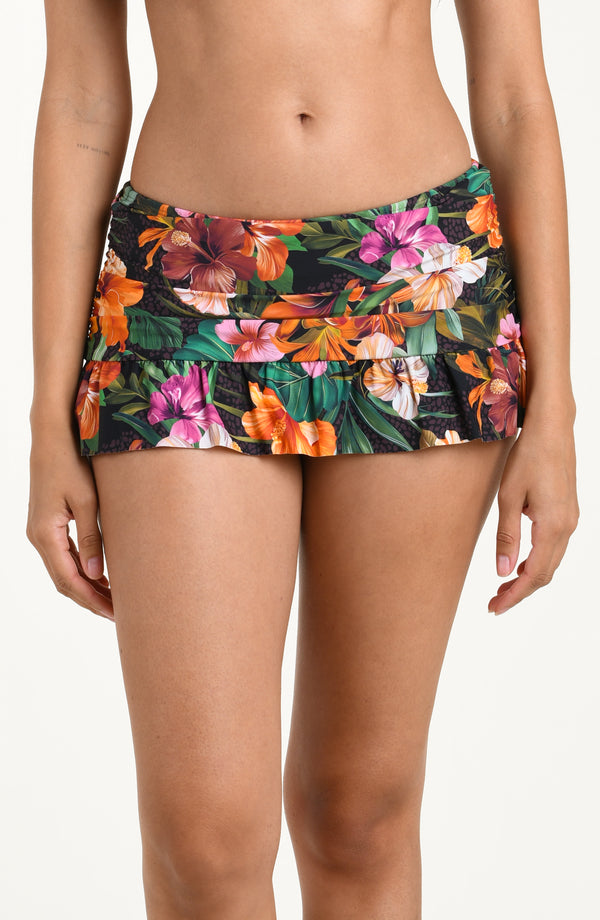 Front image of model wearing a multicolored tropical printed swim skirt with a ruched waistband and a flared ruffle hem. 