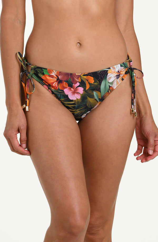 Front image of model wearing a multicolored tropical printed hipster bikini bottoms with adjustable side ties accented with gold tips.