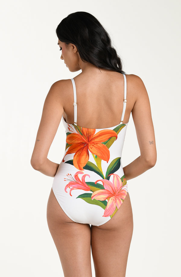 Woman wearing a white one-piece swimsuit with floral designs on a plain background