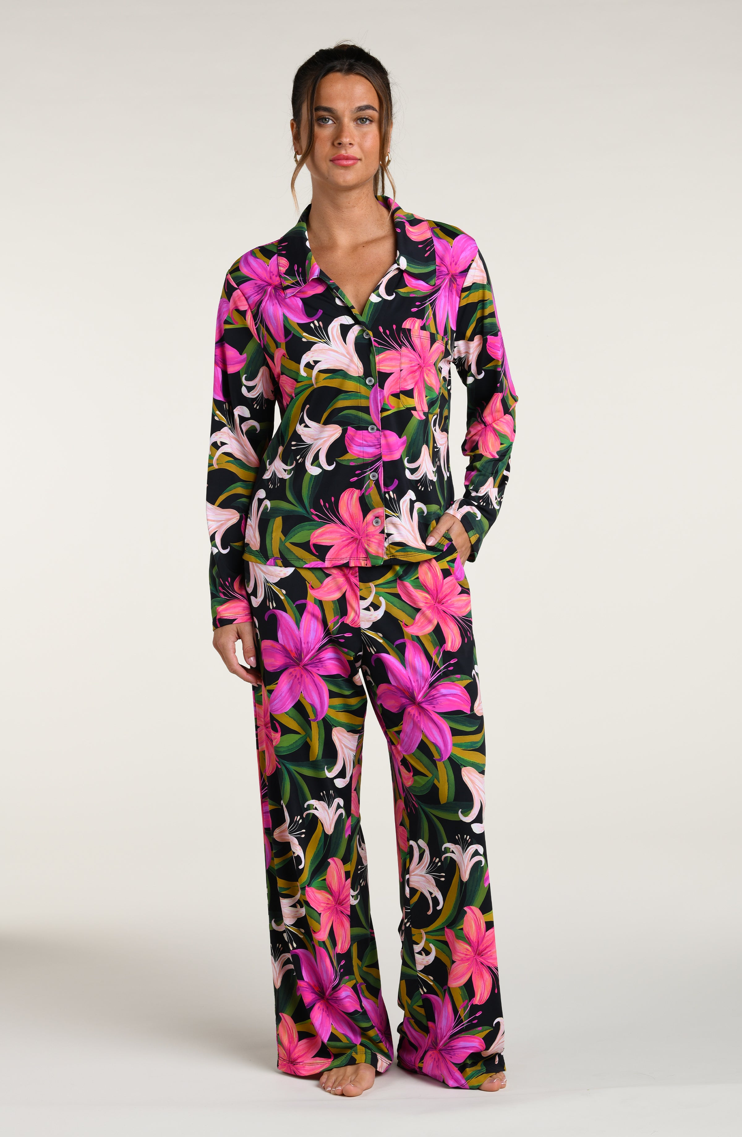 Woman wearing a colorful tropical long sleeve and pant pajama set against a white background.