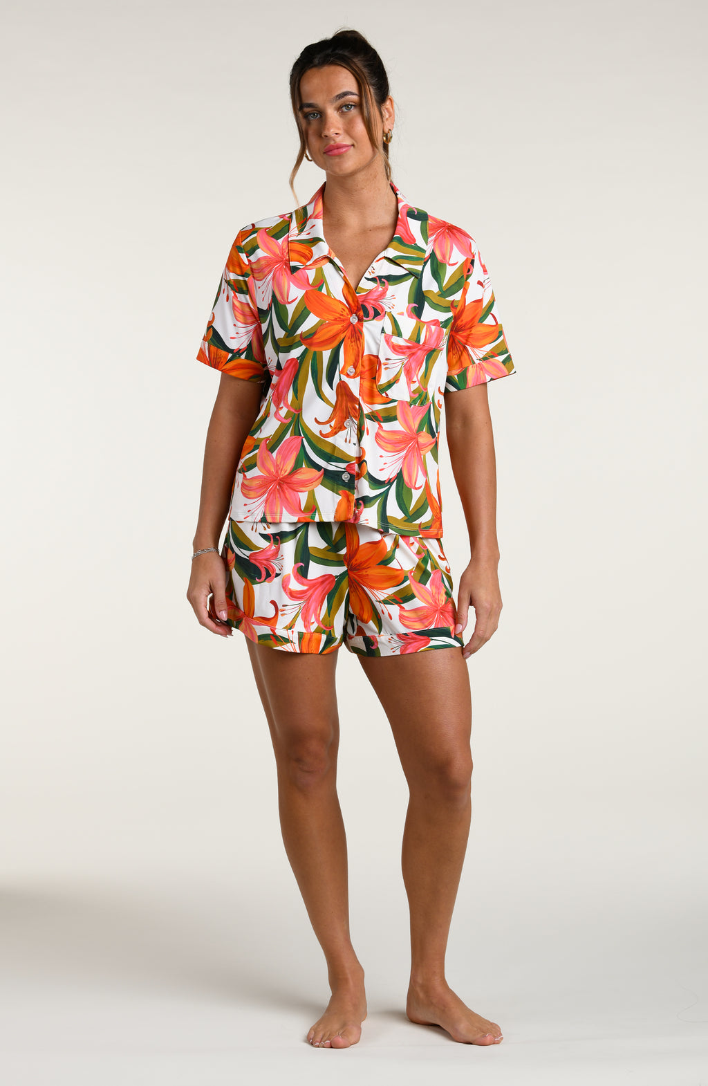 Woman wearing a colorful tropical long sleeve and short pajama set against a white background.