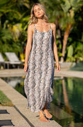 Lifestyle image of model wearing a sleeveless maxi cover-up dress with thin over the shoulder straps, pockets, and an allover taupe colored animal print.