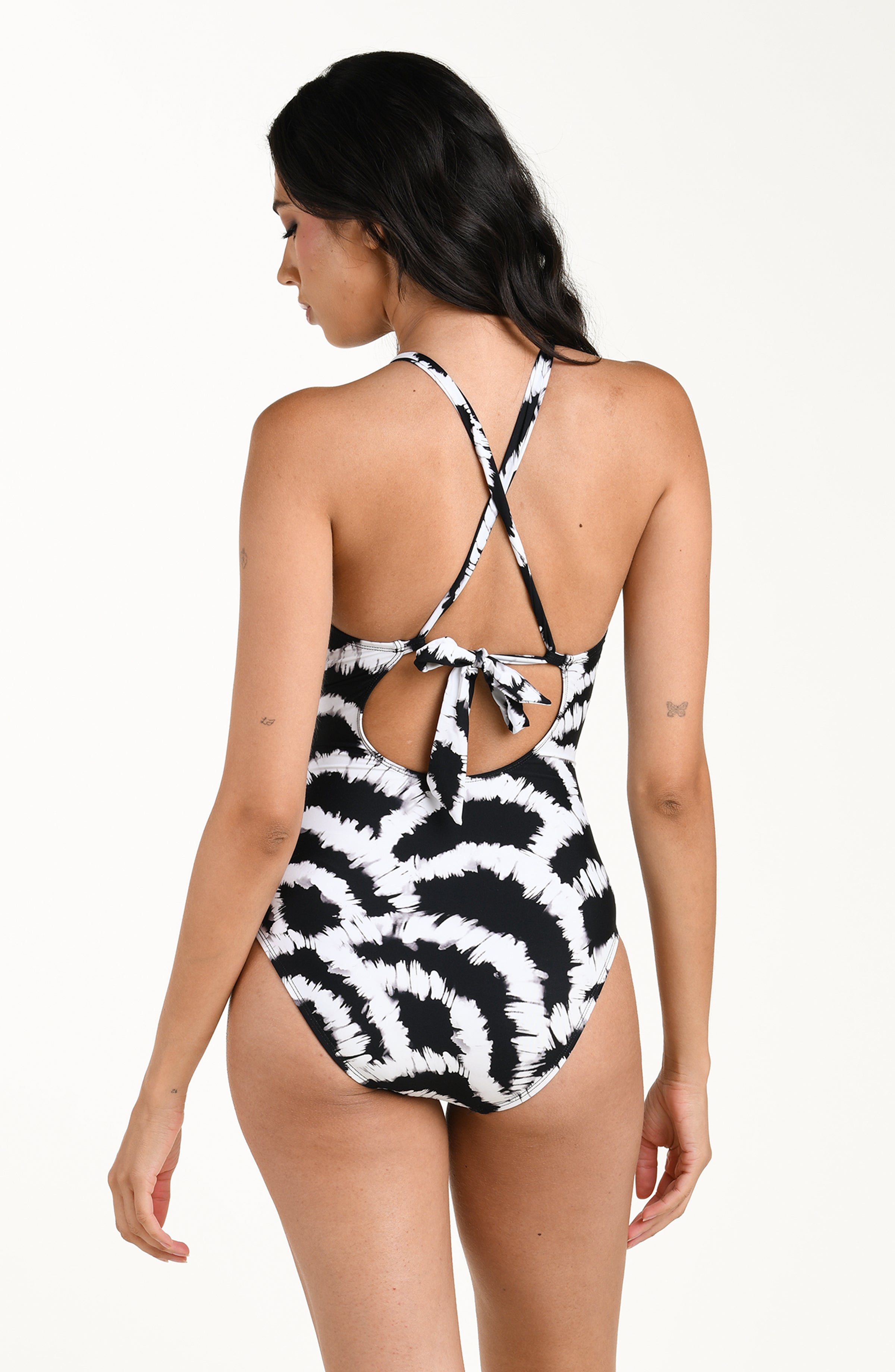 Back image of model wearing a black and white multicolored one piece swimsuit featuring a supportive, flattering fit with adjustable crisscross straps and a tie-back detail, and moderate rear coverage. 