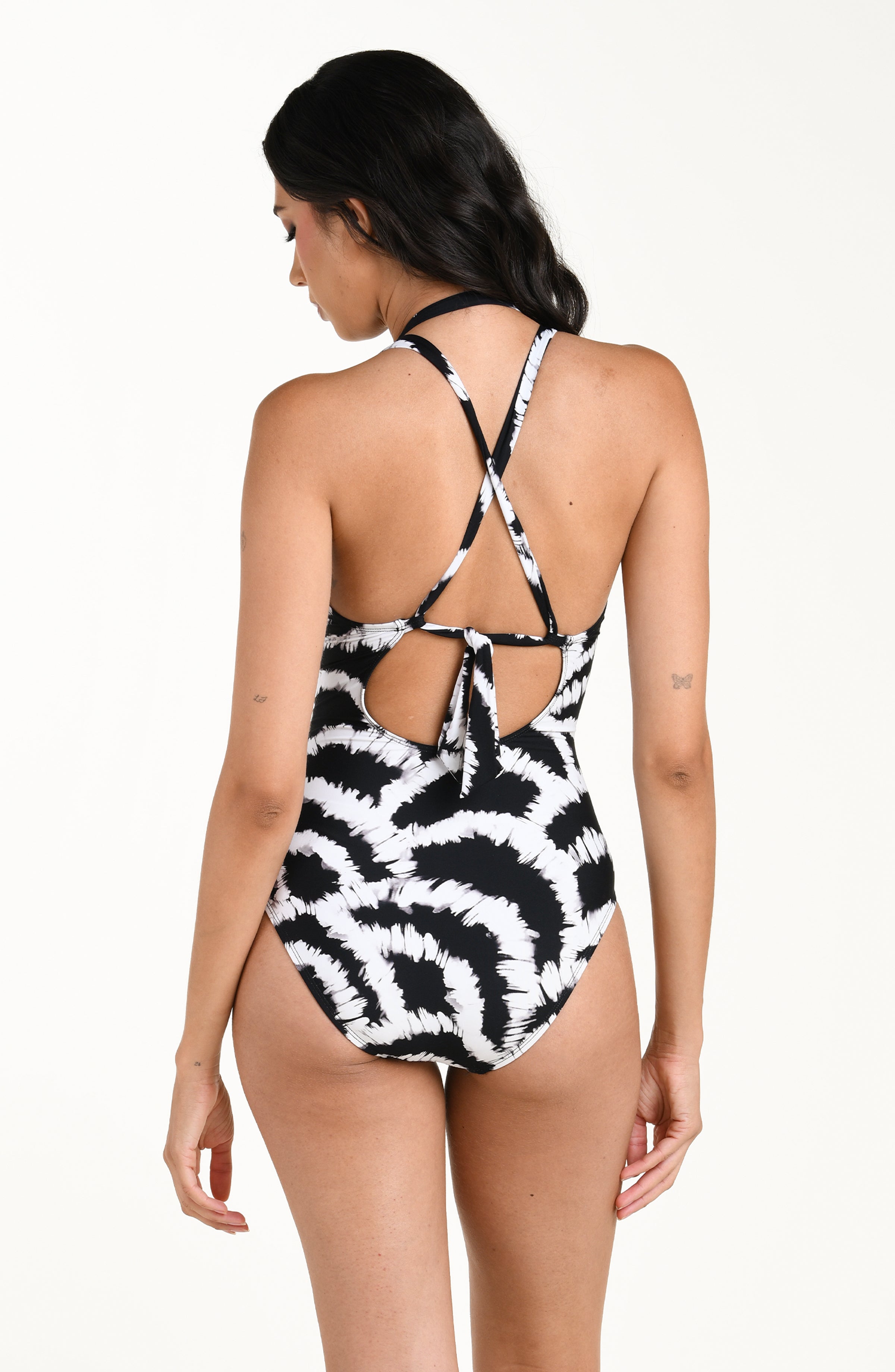 Back image of model wearing a black and white multicolored one piece swimsuit featuring a supportive, flattering fit with adjustable crisscross straps and a tie-back detail, and moderate rear coverage. 