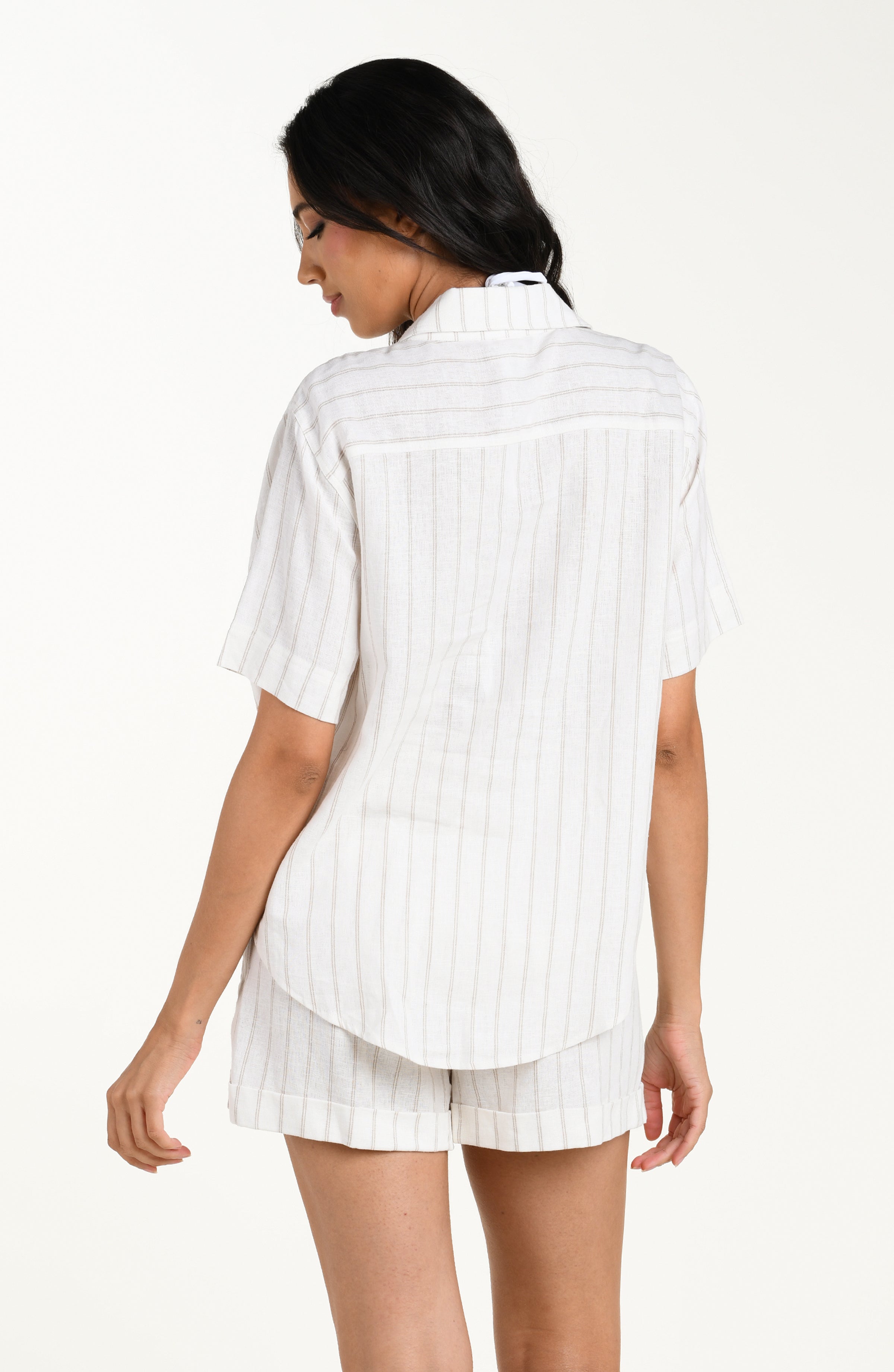 Back image of model wearing a cream striped colored short-sleeve cover-up shirt with a relaxed fit and rounded hem. It's paired with matching beach shorts.