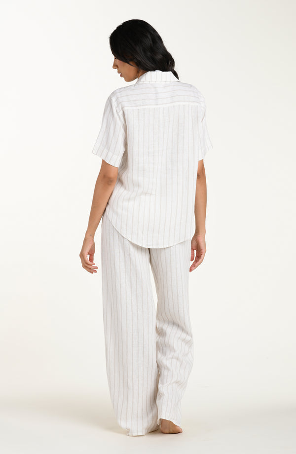 Back image of model wearing a cream striped colored short-sleeve cover-up shirt with button front, chest pocket, and tie-front waist.